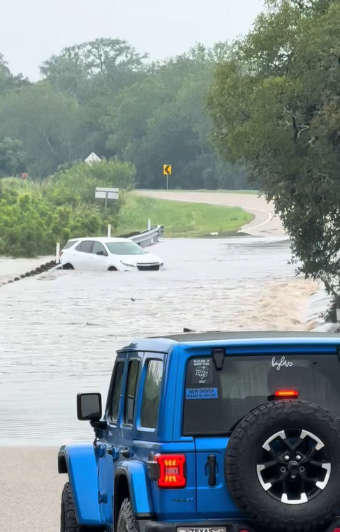 flooded road with a white SUV partially submerged in the water