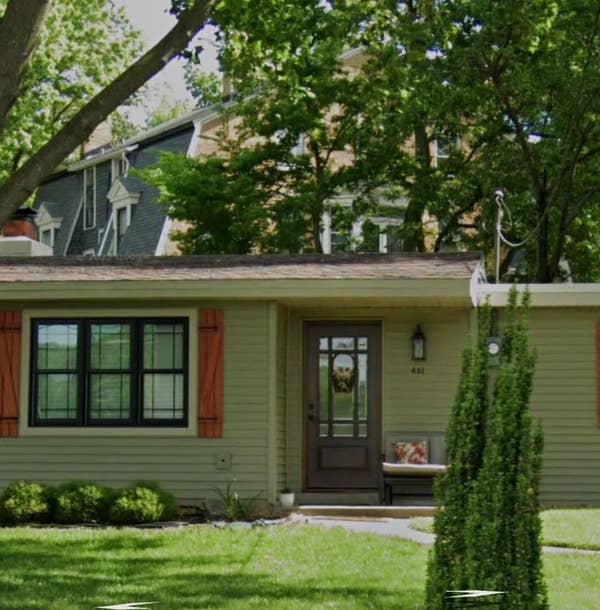A small single-story house with a front yard, shrubs, and tall tree in a suburban setting